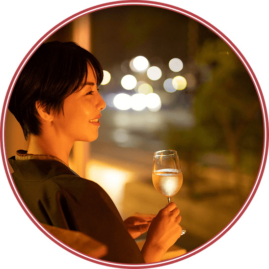 浴衣姿の女性が夜景を眺めながらグラスを手に微笑む様子